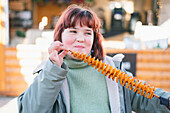 A girl enjoys a crispy tornado potato spiral at an outdoor market. The fun snack on a stick is popular for its unique shape and crunchy texture and perfect for street food lovers.