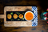 Top view of golden sweetcorn and spring onion pies, served with a bowl of sweet chilli sauce, garnished with fresh greens, beautifully arranged on a slate board over a rustic wooden table