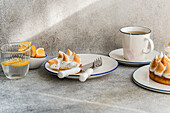 An elegantly laid table with lemon meringue tarts, a cup of tea and fresh lemon slices. Ideal for a cosy afternoon tea or brunch setting.