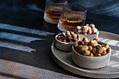 'Spiced cognac cocktail with cinnamon and aniseed, served with a variety of nuts: Almonds, peanuts and hazelnuts - beautifully arranged on a dark grey, textured surface that captures the play of light and shadow.'