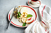 Classic homemade apple waffles with ripe apple slices, banana and mint leaves, served next to a cup of coffee on a grey surface.