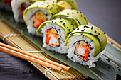 Delicious sushi rolls, elegantly wrapped with avocado slices, served on a traditional bamboo mat. The rolls are sprinkled with black sesame seeds, which give them texture and flavour.