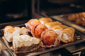A tantalising selection of pastries in the window of a bakery with cream-filled buns, sugar-coated treats and layered delicacies perfect for satisfying sweet cravings