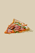 A gourmet pizza slice topped with prosciutto, sun-dried tomatoes, mozzarella, rocket, capers, oregano and parmesan, beautifully presented on a pastel yellow background.