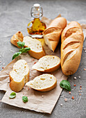 Sliced fresh, crusty baguette with salt, olive oil and basil on a grey concrete background