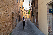 A person walks through the narrow, ancient streets of Volterra in Tuscany. Surrounded by rustic stone buildings, the scene captures the essence of Italian medieval architecture and culture