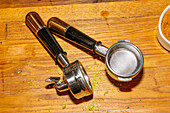 Two portafilters for espresso machines stand with their metal baskets and handles on a wooden table.