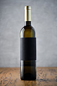 A single elegant wine bottle with an empty label stands on a wooden surface against a textured grey background, perfect for branding mockups.