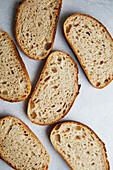 Top view of freshly sliced sourdough bread with a textured, porous interior on a grey background.