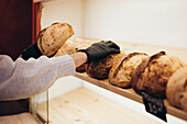 A hand reaches for freshly baked, artisan bread in a cosy bakery The loaves lie on a wooden shelf and invite you to eat them with their golden crusts and warm aromas - perfect for culinary themes