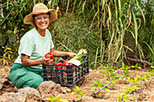 A woman in a hat smiles as she harvests fresh vegetables from her garden Young plants grow with the help of a visible drip irrigation system