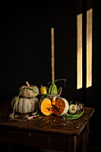 A rustic still life with pumpkins and various vegetables on a wooden table. Gentle sunlight falls through and casts soft shadows, creating a warm, autumnal ambience.