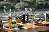 A cosy table set with snacks and red and white wine, surrounded by a sunny ambience Lively greenery and decor create an inviting atmosphere