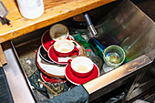 Close-up of unwashed red coffee cups in a kitchen sink, illustrating the aftermath of a busy day in a coffee shop. An insight into daily operations.