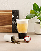 A refreshing bubble tea stands stylishly on a table, presenting its creamy layers Next to it, a glass of loose tea leaves lies open, adding an authentic touch to the scene