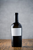 An elegant dark wine bottle with an empty label against a soft background on a wooden surface that offers space for branding.