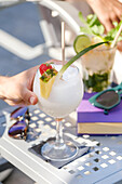 Close-up of a refreshing cocktail with pineapple, strawberries and coconut garnish on an outdoor table. Perfect for summer relaxation or holiday mood.