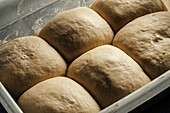 Close-up of six portions of bread dough resting in a container, emphasising their smooth texture and square shape. Perfect for themes such as baking, cooking and food preparation.