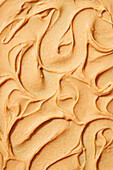 Top view of a soft peanut butter, showing its rich texture and creamy swirl. The orange-coloured spread is photographed in detail, highlighting the patterns and consistency typical of this popular raw peanut spread.