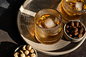Blick von oben auf einen gewürzten Cognac-Cocktail mit Zimt- und Anisstern, ergänzt durch Schalen mit Mandeln, Erdnüssen und anderen Nüssen, alles auf einem strukturierten Tablett serviert.