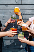 A group of friends raise their bright cocktails to a celebratory toast. The mix of refreshing drinks, garnished with citrus fruits and mint, creates a stylish and convivial atmosphere in a modern bar setting.