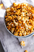 Top view of a bowl filled with crunchy caramel popcorn on a textured fabric background.