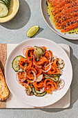 A colourful salmon salad with radishes and cucumber on a white plate, served with lime, herbs and sesame seeds for a fresh and healthy meal.