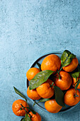 Fresh mandarins with bright green leaves arranged on a textured blue surface, creating a visually appealing contrast. Ideal for themes such as freshness and simplicity.