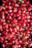 A close-up of shiny pomegranate seeds, revealing their bright red colour and translucent texture. The composition emphasises the freshness and juiciness of the fruit.