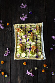 A beautifully arranged courgette tartlet, garnished with vibrant edible flowers on a dark wooden background. The arrangement is a blend of culinary art and natural beauty.