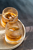 Two glasses of a spiced cognac cocktail with cinnamon and star anise, accompanied by various nuts, elegantly presented on a textured tray.