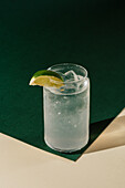 A refreshing citrus lemonade, served in a tall glass, garnished with a fresh lime wedge. The drink stands on a green and beige surface that creates a lively, summery atmosphere.