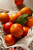 A bouquet of bright blood oranges with deep red hues lies in a reusable cotton bag on a rustic table. The fresh fruit shines in bright colours and with a natural texture.