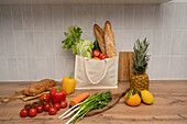 A reusable carrier bag filled with fresh produce and baguettes stands on a wooden table. Surrounded by colourful fruit and vegetables, the establishment promotes healthy, environmentally conscious living.