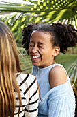 Two friends are spending a happy moment outdoors, laughing in the sun. One girl is wearing a striped shirt, the other a blue top. The scene radiates cheerfulness.