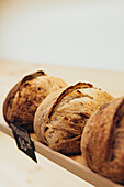 Three freshly baked loaves lie on a wooden rack in a cosy bakery. The golden crust and rustic look are reminiscent of warmth and traditional craftsmanship