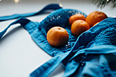 Close-up of ripe mandarins stowed in a bright blue string bag against a soft, blurred background with subtle lighting.