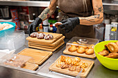 In an Italian bakery, a person arranges freshly baked pastries on wooden trays. The employee is wearing gloves, which creates a hygienic and handcrafted atmosphere.