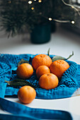 Delicious mandarins in a bright blue bag, contrasted by soft Christmas lights in the background, create a warm, festive atmosphere.