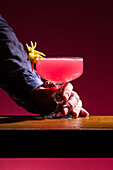 A Cosmopolitan cocktail is elegantly presented in a coupe glass decorated with a slice of lemon. The pink-coloured drink stands out beautifully against the atmospheric background and emphasises its refreshing effect