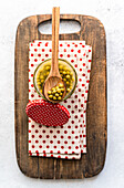A preserving jar of homemade organic peas with a wooden spoon on a rustic wooden board. The jar stands on a dotted napkin with a matching lid next to it, creating a cosy kitchen atmosphere.