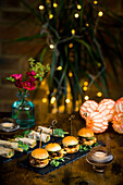 Beautifully designed food presentation with vegetable and courgette rolls alongside pulled pork and cabbage mini burgers The slate tables, candlelight and floral decorations create a festive ambience
