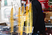 Close-up of spiral-shaped Tornado potatoes on sticks on sale at an outdoor market. The bright yellow spirals make a visually appealing snack presentation.
