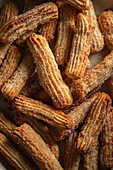 Top view of freshly baked churros sprinkled with sugar, piled up in a ceramic bowl and sprinkled with cinnamon, creating a cosy, homemade dessert with an atmospheric ambience