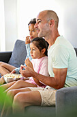 A family of three sits on a comfortable sofa, engrossed in a film and sharing a bowl of popcorn. The atmosphere is relaxed and cosy, and family time is a priority.