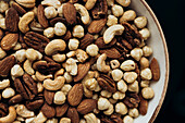 A close-up of various nuts, including almonds, cashews, hazelnuts and pecans, filling a ceramic bowl - perfect for healthy snacks or adding flavour to your favourite recipes