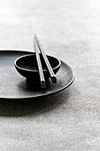 A minimalist placemat in black and white with a plate, a bowl and chopsticks. The composition emphasises simplicity and elegance and is suitable for modern dining aesthetics.