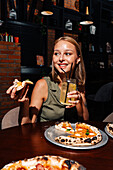 A cheerful person enjoys a slice of Margherita pizza with a glass of refreshing lemonade. The scene takes place in a cosy restaurant where relaxation and culinary delights take centre stage.
