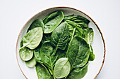 A bowl of fresh green spinach leaves glistening with drops of water. The bright colours and natural freshness of the leaves are perfect for a healthy lifestyle theme.