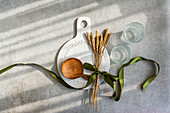 A stylish table setting with a white ceramic plate, wheat stalks tied with a green ribbon, a wooden board and glass cups - perfect for rustic or nature-inspired themes
